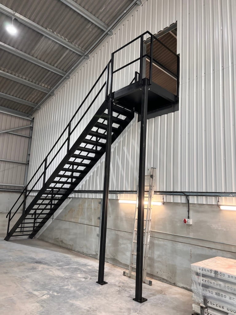 Internal steel staircase in an agricultural building leading to a doorway cut out in an internal wall.