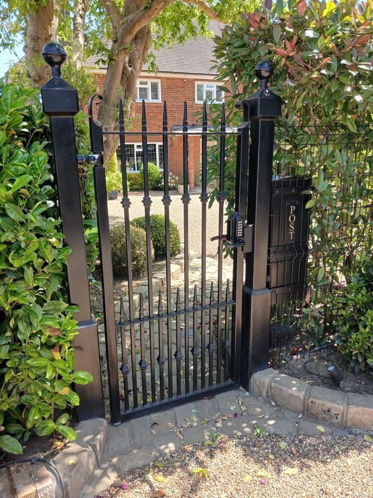 A decorative metalwork pedestrian gate to the side of a residential property fabricated from steel with a black powder coated finish and an inverted arch top